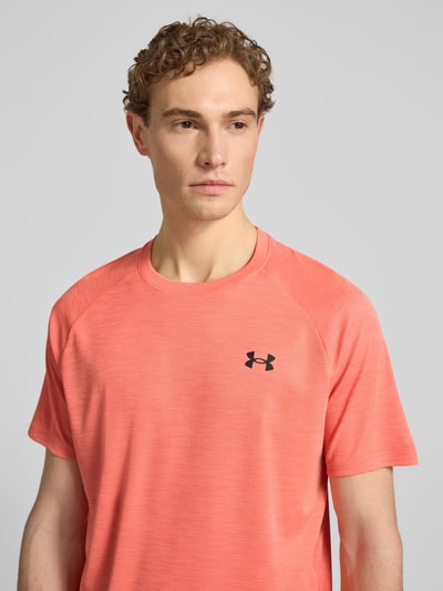 Männermodel trägt T-Shirt mit Label-Print Modell 'Tech' von Under Armour in Koralle, Gerader-Schnitt, Rundhalsausschnitt, Nahaufnahme Oberkörper, Rückenlänge bei Größe M: 75 cm.
