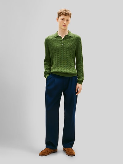 Männermodel trägt Regular Fit Strickpullover aus reiner Baumwolle von Tommy Hilfiger in Grün mit Zopfmuster, unifarben, Ganzkörperansicht von vorne.