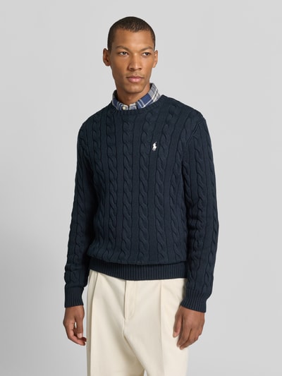 Männermodel trägt Pullover mit Logo-Stitching von POLO RALPH LAUREN in Dunkelblau, Zopfmuster, unifarben, Rippenbündchen, Ganzkörperansicht von vorne.