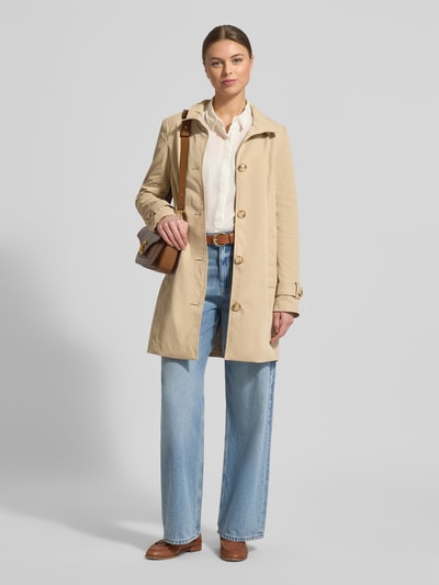 Frauenmodel trägt Trenchcoat mit Stehkragen und Ärmelriegeln von Christian Berg Woman Selection in Beige, glatte Oberfläche, Ganzkörperansicht von vorne.
