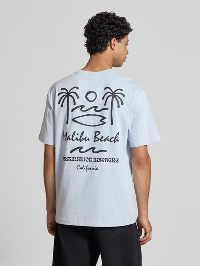Männermodel trägt Relaxed Fit T-Shirt aus reiner Baumwolle Modell 'MILO' von Only & Sons, hellblau mit schwarzem Print, Ganzkörperansicht Rückansicht.