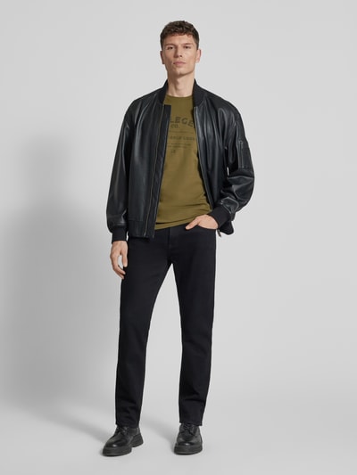 Männermodel trägt Regular Fit T-Shirt mit Logo-Print von PME Legend in Olivgrün, schwarze Hose, schwarze Jacke, Ganzkörperansicht von vorne. Reine Baumwolle, Rundhalsausschnitt, Rückenlänge bei Größe M 74 cm.