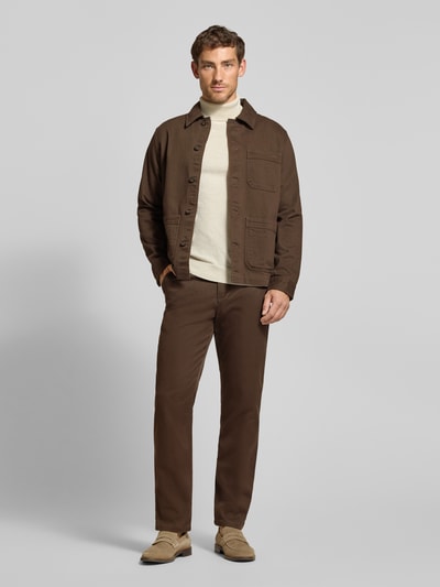 Männermodel trägt Straight Fit Chino aus Baumwoll-Mix Modell 'Miles' von Selected in Braun, kombiniert mit beigefarbenem Pullover, Ganzkörperansicht von vorne, Herren Chino von Selected.