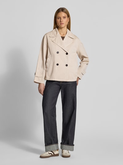 Modelka nosi Regular Fit Trenchcoat aus reiner Baumwolle von Marc O'Polo, jednolity, krój regular fit, dwurzędowe zapięcie, długi rękaw z paskiem, boczne kieszenie, materiał bawełniany, jasnobeżowy, przód, pełna sylwetka
