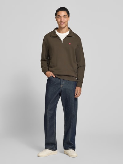 Männermodel trägt Regular Fit Troyer aus reiner Baumwolle von Levi's® in Olivgrün, kombiniert mit Jeans, Ganzkörperansicht von vorne.