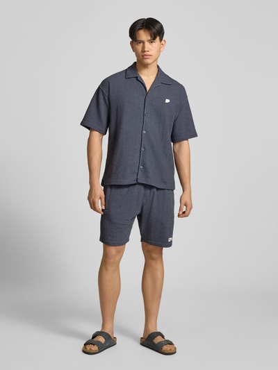 Männermodel trägt Herren Shorts mit Label-Patch Modell 'LIBCO' von Pegador im Strukturmuster Material-Mix, Farbe Dunkelblau, Gerader-Schnitt, elastischer Bund, Ganzkörperansicht von vorne.