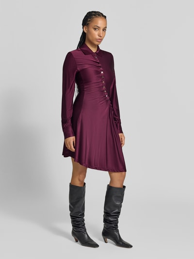Frauenmodel trägt Knielanges Kleid aus Viskose-Mix von Rabanne in Dunkelrot mit Umlegekragen, Knopfleiste und langen Ärmeln, tailliert, Stoff glänzend, Ganzkörperansicht von vorne.