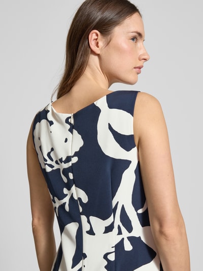 Frauenmodel trägt knielanges Cocktailkleid in Wickel-Optik von Vera Mont mit Rundhalsausschnitt, elastischer Material-Mix, Ziernähte, abstraktes navy-weißes Muster, taillierte Passform, Nahtreißverschluss hinten, Nahaufnahme Rückansicht.