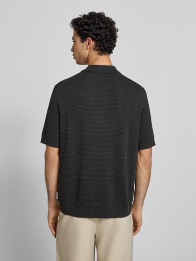 Männermodel trägt Regular Fit Poloshirt aus reiner Baumwolle von Marc O'Polo Denim, schwarz, Strickstruktur, Label Patch, Ganzkörperansicht Rückansicht