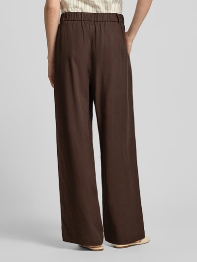 Frauenmodel trägt Wide Fit Leinenhose mit elastischem Bund von comma, Dunkelbraun, lockerer Schnitt, feine Drapierungen, reine Leinenstruktur, Ganzkörperansicht Rückansicht.