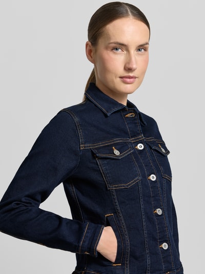 Frauenmodel trägt Slim Fit Jeansjacke aus Baumwoll-Mix von Tom Tailor in Dunkelblau mit Umlegekragen, Label-Prägung, Kontrastnähten, seitlichen Eingrifftaschen und Brusttaschen, Denim-Optik, Materialverarbeitung Twill, Nahaufnahme Oberkörper.
