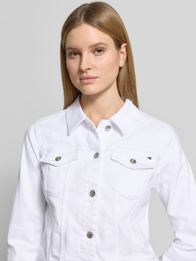 Kobiece model prezentuje Slim Fit Jeansjacke aus Baumwoll-Mix von Tommy Hilfiger, biała dżinsowa twillowa kurtka z kołnierzem, naszywką z logo, kieszeniami na piersiach i po bokach, krój slim fit, materiał bawełniany-mieszanka; zbliżenie na górną część ciała od przodu.