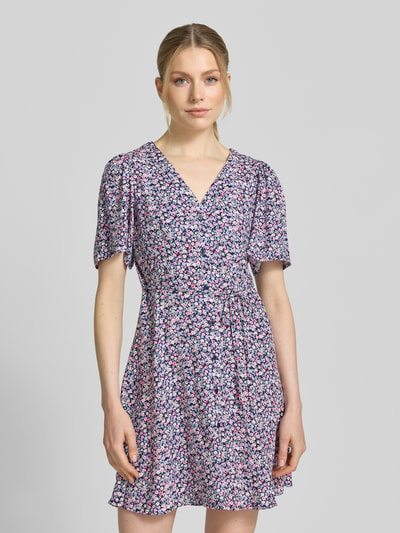 Frauenmodel trägt Leicht ausgestelltes Minikleid aus reiner Viskose Modell 'ALBA' von Vero Moda in Optik: Unifarben, Kurzarm, Mini-Länge, V-Ausschnitt, Taillengürtel, Knopfleiste, Material: Reine Viskose, Ganzkörperansicht von vorne.