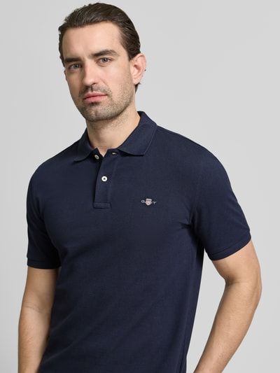 Męski model ma na sobie Slim Fit Poloshirt mit Logo-Stitching od Gant, ciemnogranatowa bawełna, krój slim fit, logo, polo kołnierzyk, koszulka z krótkim rękawem, długość tyłu w rozmiarze M: 70 cm, widok na górną część ciała z przodu.