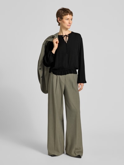 Frauenmodel trägt Bluse aus Viskose mit Schlüsselloch-Ausschnitt von Emily Van den Bergh in Schwarz, lockerer Schnitt, weite helle Hose, Ganzkörperansicht von vorne.