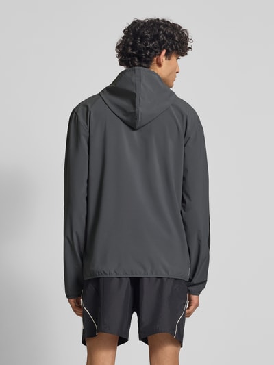 Männermodel trägt Slim Fit Funktionsjacke aus schnelltrocknendem Material von adidas Sportswear, efekt: jednolity kolor, krój slim fit, kaptur, zamek błyskawiczny, nadruk z logo, paski w kontrastowym kolorze, długi rękaw, szybkoschnący, materiał pochłaniający pot, boczne kieszenie zapinane na zamek błyskawiczny, Ganzkörperansicht Rückansicht.