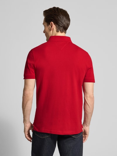 Męski model nosi Regular Fit Poloshirt aus Baumwoll-Mix od Tommy Hilfiger, czerwony, bawełniany pikowany materiał, gładki, krój regular fit, rozcięcia po bokach, haftowane logo, całkowity widok z tyłu