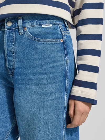 Frauenmodel trägt High Waist Barrel Jeans aus reiner Baumwolle Modell 'BAARLY' von Armedangels in Denim-Optik mit 5-Pocket-Design, Label-Patch, Nieten, Knopf und verdecktem Reißverschluss, leicht strukturierte, mittlere blaue Farbe, Nahaufnahme Oberkörper.