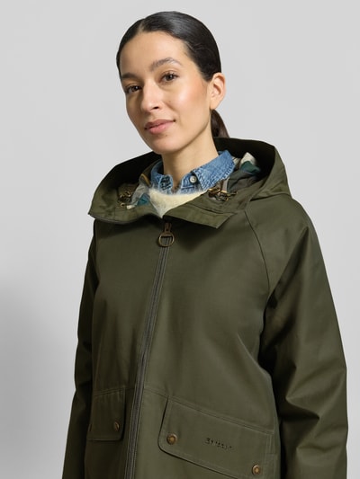 Kobiece model prezentuje Regular Fit Parka aus Baumwoll-Mix od Barbour, jednokolorowy, krój regular fit, z kapturem na tunel, zamek błyskawiczny dwustronny, z napisem z logo, pas na plecach, długi rękaw, proste wykończenie, hydrofobowy, oddychający materiał, kieszenie wpuszczane, kieszenie z patką, kieszeń wewnętrzna, mieszanka bawełny; zbliżenie na górną część ciała.