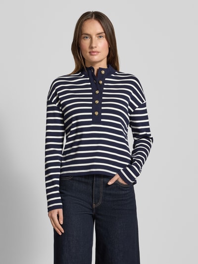 Frauenmodel trägt Ringel Polo Shirt mit Schmuckknopf von Christian Berg Woman, dunkelblau-weiß gestreift, gerippter Stehkragen, lockerer Schnitt, Nahaufnahme Oberkörper.