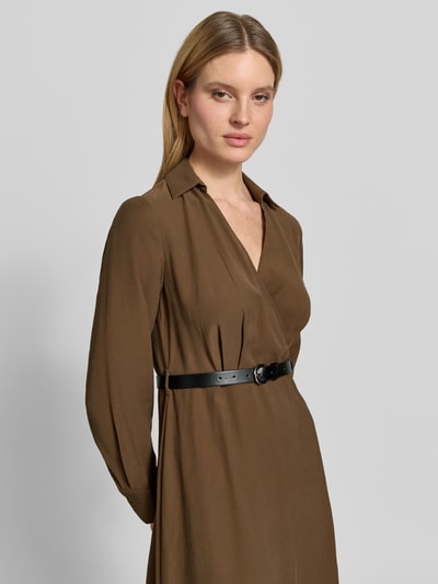 Modelka kobieca nosi sukienkę midi w kopertowym stylu z paskiem marki Jake*s Collection, mieszanka wiskozy, linia a, wykładany kołnierz, dekolt w serek, pasek, długość tyłu w rozmiarze 36: 128 cm, szerokość w rozmiarze 36: 37 cm, długość rękawów w rozmiarze 36: 62 cm, odcień brązu, gładka tekstura, półzbliżenie górnej części ciała, widok z przodu.