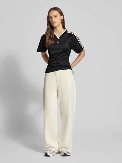 Vrouwenmodel draagt T-Shirt met V-Ausschnitt van adidas Originals in zwart met asymmetrisch design, aansluitende fit, detailopname volledige voorkant