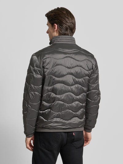 Männermodel trägt Steppjacke mit Reißverschluss von Guess in Grau mit Stehkragen, gerippten Abschlüssen, Regular Fit, Ganzkörperansicht Rückansicht.