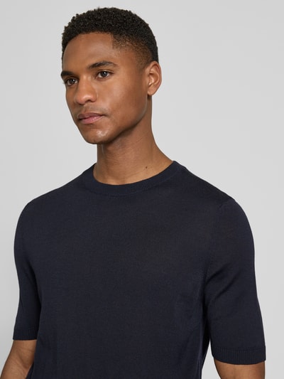 Männermodel trägt donkerblau 'Strickshirt mit Rundhalsausschnitt' van MAERZ Muenchen, slim fit, ribboorden, labeldetail, halve mouwen, Nahaufnahme Oberkörper.