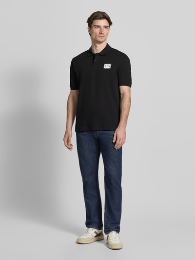 Mannenmodel draagt Regular Fit Poloshirt met knoopsluiting van Armani Exchange in zwart, mix van katoen en elastaan, labelprint, regular fit, polokraag met knoopsluiting, elastische mouwboordjes, ruglengte maat M 70 cm, geheel van voren te zien.