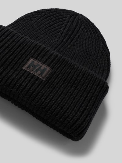 Produktfoto, Beanie in Strick-Optik mit Logo-Patch von Helly Hansen in Schwarz, grobes Strukturmuster, fixierter Bund, neutraler Hintergrund