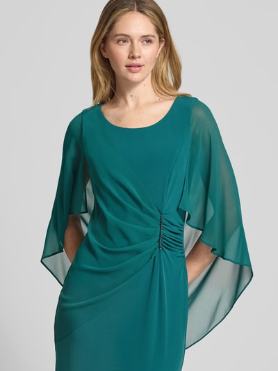 Modelka nosi Knielanges Cocktailkleid mit Rundhalsausschnitt von Vera Mont, elastyczna mieszanka materiałów, dopasowany krój, okrągły dekolt, kopertowy styl, ozdobna aplikacja z obszyciem z kamieni stras, długość do kolan, wszyty zamek błyskawiczny z tyłu, rękawy nietoperzowe z szyfonu, długość tyłu w rozmiarze 36: 98 cm, szerokość w rozmiarze 36: 108 cm, długość rękawów w rozmiarze 36: 48 cm, całość w kolorze zielonym, widoczne gładkie powierzchnie i lekki połysk materiału, całkowite ujęcie przodu górnej części sylwetki