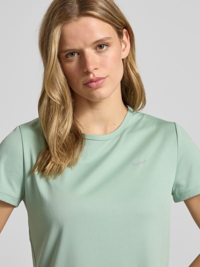 Modelka nosi damski t-shirt z logo, model 'Tempo' od NIKE TRAINING, krój regular fit, okrągły dekolt, kolor jasny zielony, długość tyłu w rozmiarze S: 56 cm, zbliżenie na górną część ciała.