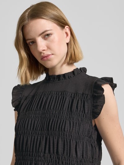 Frauenmodel trägt Blusentop mit Rüschenkragen Modell 'CATH' von Soyaconcept, Struktur durch Smok-Detail, Schwarz, Nahaufnahme Oberkörper. Körpernaher-Schnitt, Rüschenärmel, Rückenlänge 60 cm, Ärmellänge 5 cm.