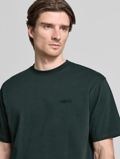 Männermodel trägt Regular Fit T-Shirt aus reiner Baumwolle Modell 'Baine' von WOODBIRD in Dunkelgrün, Nahaufnahme Oberkörper.