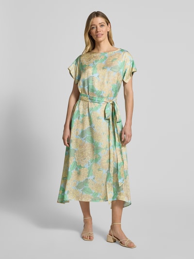 Frauenmodel trägt Midikleid aus Viskose mit Bindegürtel von Rich & Royal, Reine Viskose, Taillierter Schnitt, U-Boot-Ausschnitt, floral gemustert, sanfte Grün- und Beigetöne, geschmeidige Textur, Rückenlänge 123 cm, Brustweite 50 cm, Ärmellänge 9 cm, Ganzkörperansicht von vorne.