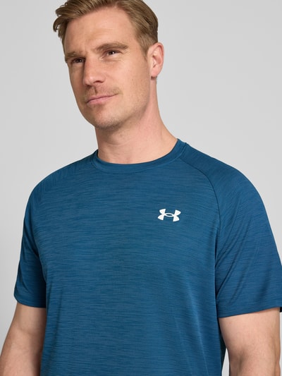 Męski model nosi T-Shirt mit Label-Print Modell 'Tech' von Under Armour w kolorze niebieskim, prosty krój, okrągły dekolt, długość tyłu w rozmiarze M: 75 cm, zbliżenie górnej części ciała.