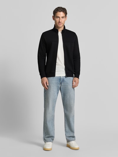 Männermodel trägt Regular Fit Sweatjacke aus Baumwoll-Mix von s.Oliver RED LABEL in Schwarz, kombiniert mit Jeans, Ganzkörperansicht von vorne.
