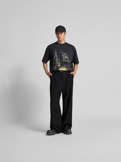 Męski model nosi Straight Fit Hose aus Schurwoll-Mix von VETEMENTS, czarne, zakładki w pasie, kieszenie z tyłu, elastyczna mieszanka żywej wełny, zapięcie na haftkę i zamek błyskawiczny, długość wewnętrzna nogawki 77 cm, szerokość w rozmiarze M 44 cm, spodnie z prostymi nogawkami, widok całej sylwetki z przodu