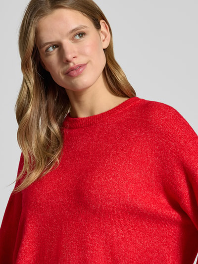 Frauenmodel trägt Relaxed Fit Strickpullover mit Crew Neck Modell 'SIMONI' von Only in roter Melange-Optik, Nahaufnahme Oberkörper.