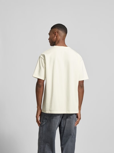 Männermodel trägt Relaxed Fit T-Shirt mit Motiv-Print von RHUDE in Creme, reine Baumwolle, kurzärmelig, Rückansicht Ganzkörperansicht.