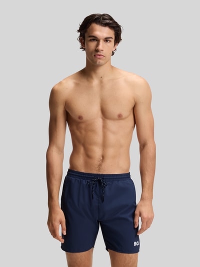 Männermodel trägt Badeshorts mit Kontrast-Logo Modell 'STARFISH' von BOSS in Dunkelblau, elastischer Bund, Ganzkörperansicht von vorne.