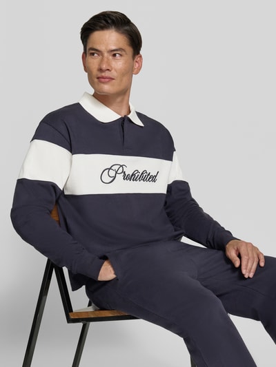 Männermodel trägt Sweatshirt aus reiner Baumwolle von PROHIBITED in Dunkelblau mit weißem Streifen und Label-Stitching, Nahaufnahme Oberkörper. Lockere Passform, Polo-Kragen, elastische Abschlüsse, Kontext: Rückenlänge 65 cm, Ärmellänge 79 cm.