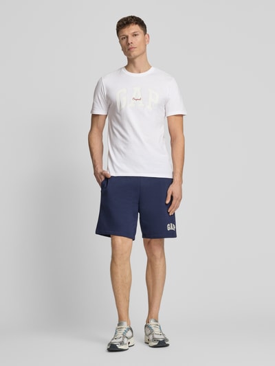Mannelijk model draagt T-shirt met logo en ronde hals van GAP, puur katoen, regular fit, ruglengte maat M 69 cm, geheel lichaam vooraanzicht.