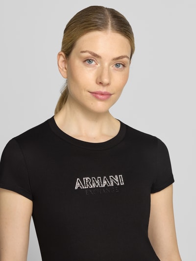 Frauenmodel trägt Slim Fit T-Shirt aus Baumwolle von Armani Exchange, Schwarz mit Strasssteinbesatz, Nahaufnahme Oberkörper.