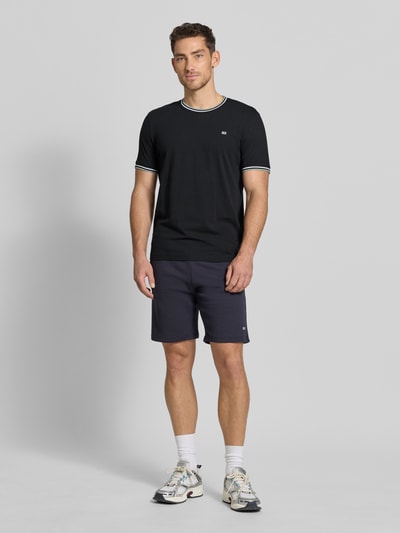 Männermodel trägt T-Shirt mit Kontraststreifen und Rundhalsausschnitt von Christian Berg Men, Baumwoll-Elasthan-Mix, Regular-Fit, Rückenlänge 71 cm, Größe M, dunkler Farbton mit schlichten Konturen, Ganzkörperansicht von vorne.