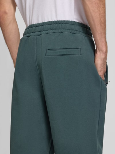 Männermodel trägt Loose Fit Sweatpants aus Baumwoll-Mix mit Label-Detail von PEGADOR in Dunkelgrün, elastischer Bund, Eingrifftaschen, Detailaufnahme Rückansicht.