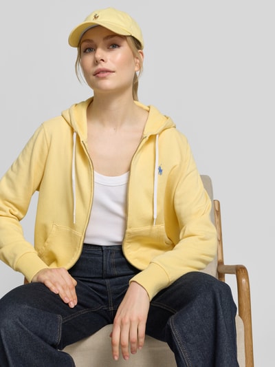 Modelka kobieca nosi Regular Fit Sweatjacke aus Baumwoll-Mix od Polo Ralph Lauren, kolor żółty, bawełna, logo z przodu, krój regular fit, kaptur, zamek, długie rękawy, dzianina, jedwabista faktura, widok na cały górny korpus z przodu.