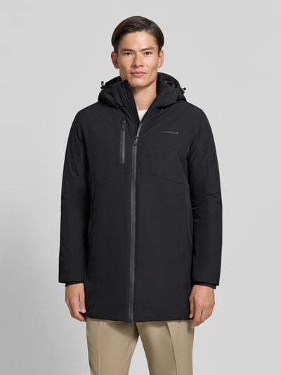 Męski model nosi Regular Fit Parka mit Logo-Print od Lindbergh, czarny kolor, elastyczna mieszanka materiałów, kaptur z tunelem, kieszeń napoleonka, zamek błyskawiczny, długość tyłu w rozmiarze M 90 cm, szerokość ramion w rozmiarze M 50 cm, szerokość w rozmiarze M 58 cm, długość rękawów 65 cm, widok całej sylwetki od przodu.