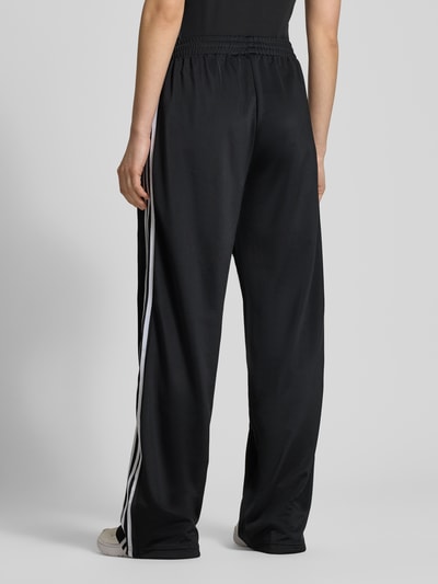 Frauenmodel trägt Sweatpants mit elastischem Bund von adidas Originals in Schwarz mit weißen Streifen, Lockerer-Schnitt, Reißverschlusstaschen, Label-Stitching, Innenbeinlänge bei Größe S 79 cm, Ganzkörperansicht Rückansicht.