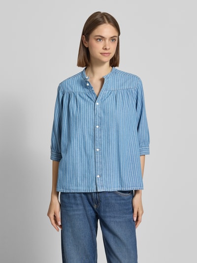 Frauenmodel trägt Regular Fit Bluse aus reiner Baumwolle Modell 'LIVIA' von Pepe Jeans in Denim-Optik, hellblau mit weißen Streifen, Maokragen und 3/4-Arm, Ganzkörperansicht von vorne.